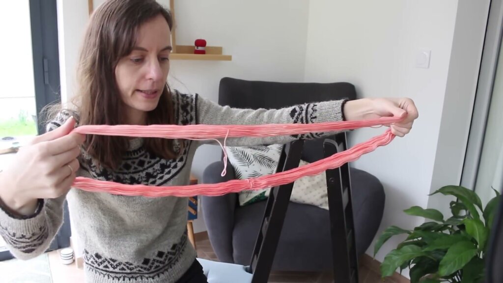 Un écheveau de laine rose tenu ouvert à deux mains, formant un grand cercle de fil