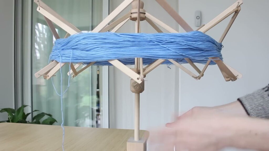 Écheveau de laine bleue tendu sur un dévidoir parapluie en bois