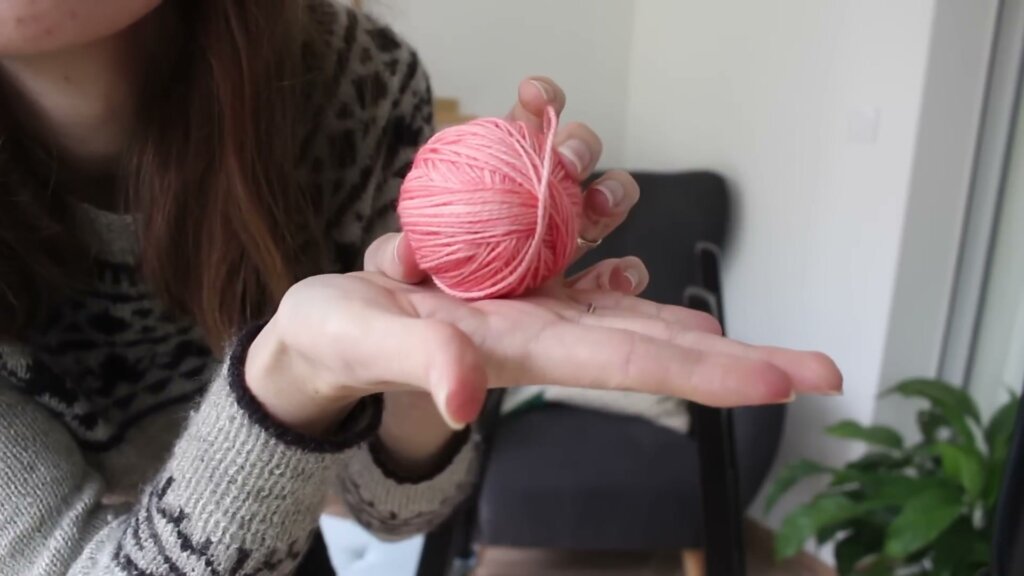 Petite pelote de laine rose enroulée à la main, tenue au creux de la main