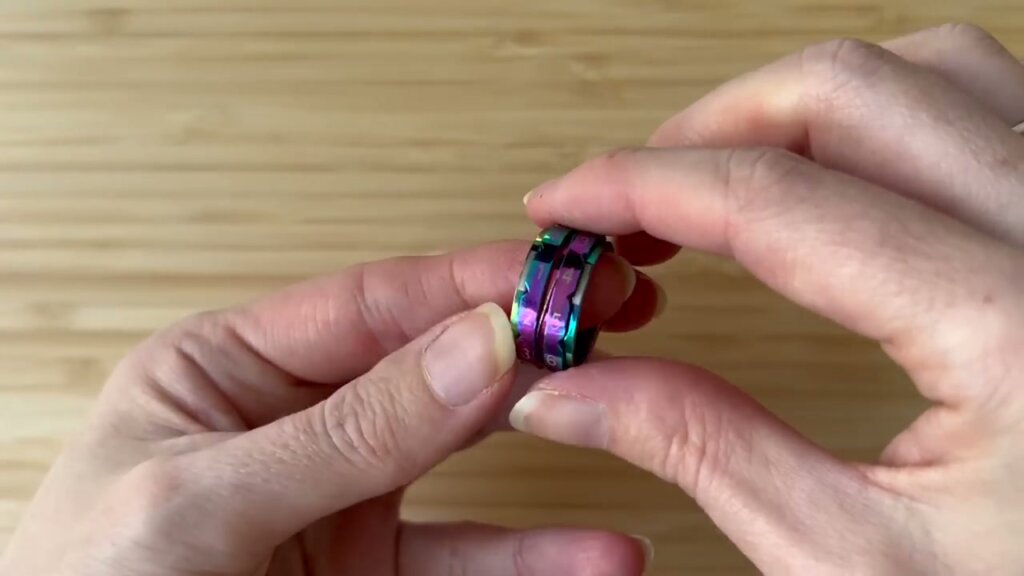 Bague compte-rangs métallique irisée tenue entre les doigts, avec des chiffres gravés pour compter les rangs