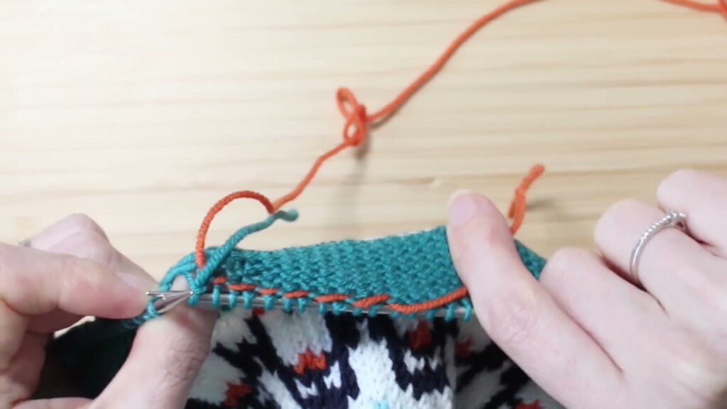 Envers du tricot montrant le fil orange croisé et coincé sous les mailles, en train d'être intégré