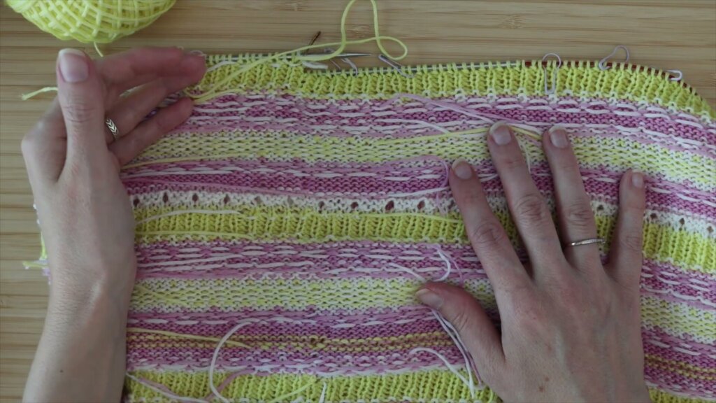 Envers d'un jacquard rose, jaune et blanc à plat, avec de nombreux bouts de fil qui dépassent après avoir été rentrés pendant le tricot